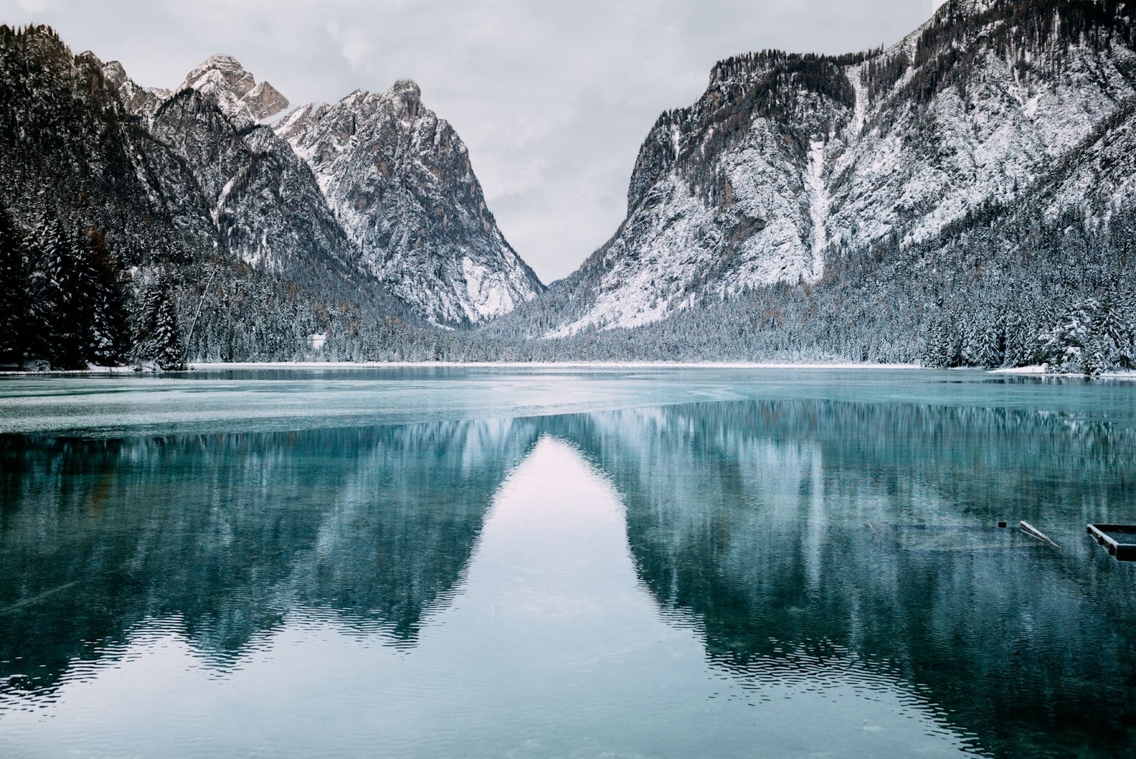 Winter is generally the “off-peak season” for travel blogging since most travelers are coming off a busy summer season of travel and want to avoid traveling to popular destinations when it is cold and snowy. A landscape featuring snow-dusted grey mountains reflecting in a blue lake, with snow-covered pine trees in front of the mountain range.